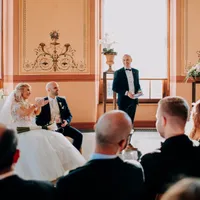 Trauredner steht lächelnd neben dem Brautpaar im Saal
