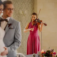 Violinistin im roten Kleid hinter unscharfem Brautpaar