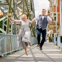 Brautpaar springt lachend über eine Stahlbrücke