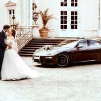 Brautpaar neben Hochzeitsauto vor hellem Schloss