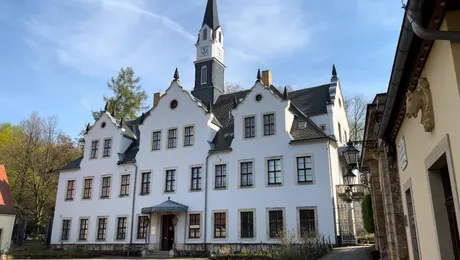Weiße Schlossfassade von Schloss Burgk mit Uhrturm unter blauem Himmel