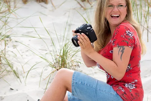 Astrid Flohr sitzt lachend mit Kamera im Dünensand