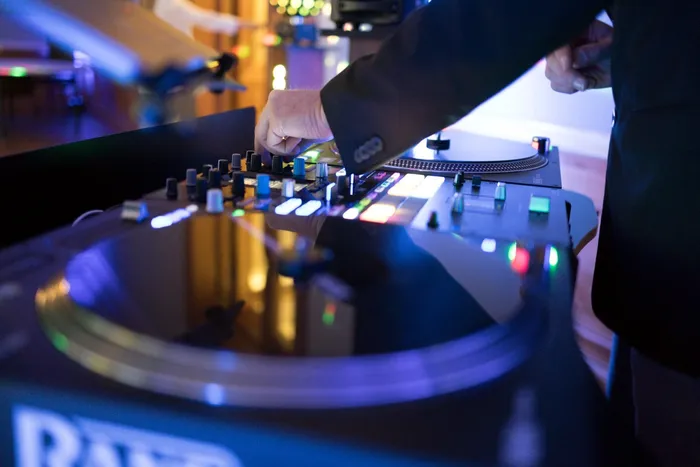 Hände am DJ-Mixer mit Plattenteller und beleuchteten Tasten