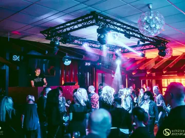 DJ am Pult vor tanzenden Gästen im Clubsaal
