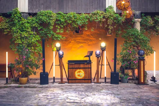 Beleuchtetes DJ-Pult aus Holz mit SJ-Logo, Lautsprechern und Lichttechnik in einem Innenhof mit Kletterpflanzen