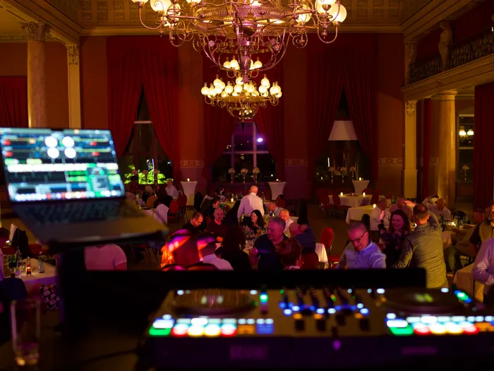 Blick vom DJ-Pult über die Gäste in einen Saal mit Kronleuchter
