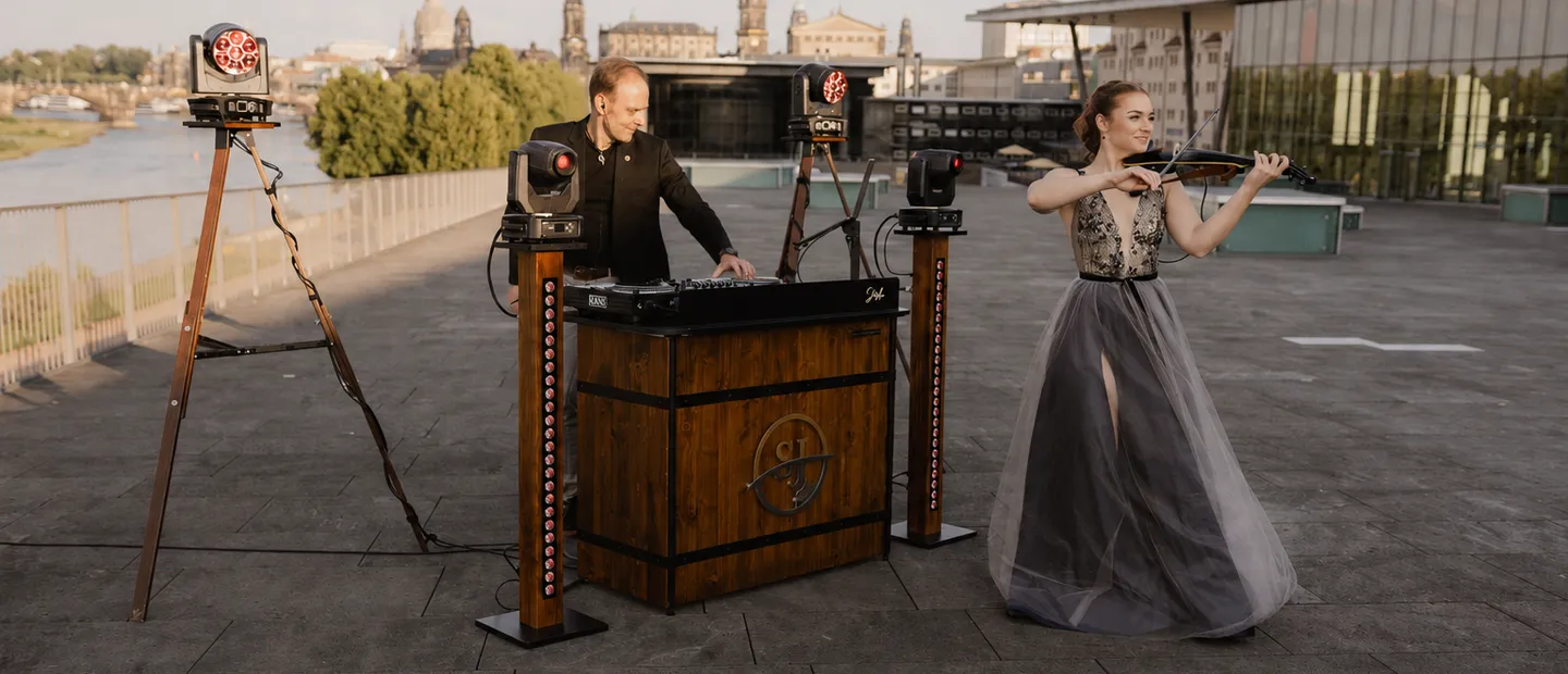 DJ-Pult mit Lichttechnik und eine Geigerin auf der Elbterrasse am Congress Center Dresden, dahinter die Silhouette der Altstadt