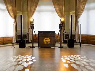DJ-Pult mit leuchtendem SJ-Logo in einem Festsaal, auf dem Boden Herzen aus Licht