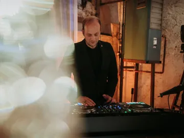 DJ Sascha Juranek am Pult vor einer Bruchsteinwand, im Vordergrund ein unscharfer Lichtschleier