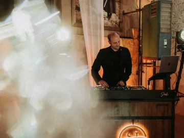 DJ Sascha Juranek beim Auflegen an seinem beleuchteten Pult vor einer Bruchsteinwand
