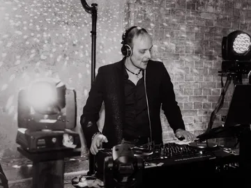 DJ Sascha Juranek mit Kopfhörern beim Auflegen vor einer Backsteinwand mit Lichtpunkten, Schwarzweißfoto