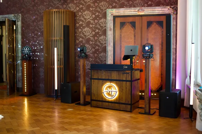 Aufgebautes DJ-Pult mit Ton- und Lichttechnik in einem Saal mit Parkett und historischer Tapete