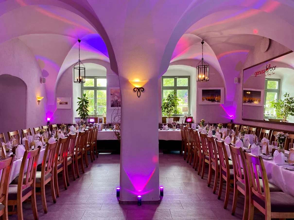 Eingedeckte Tafeln im Gewölbesaal der Genussbar in violettem Licht