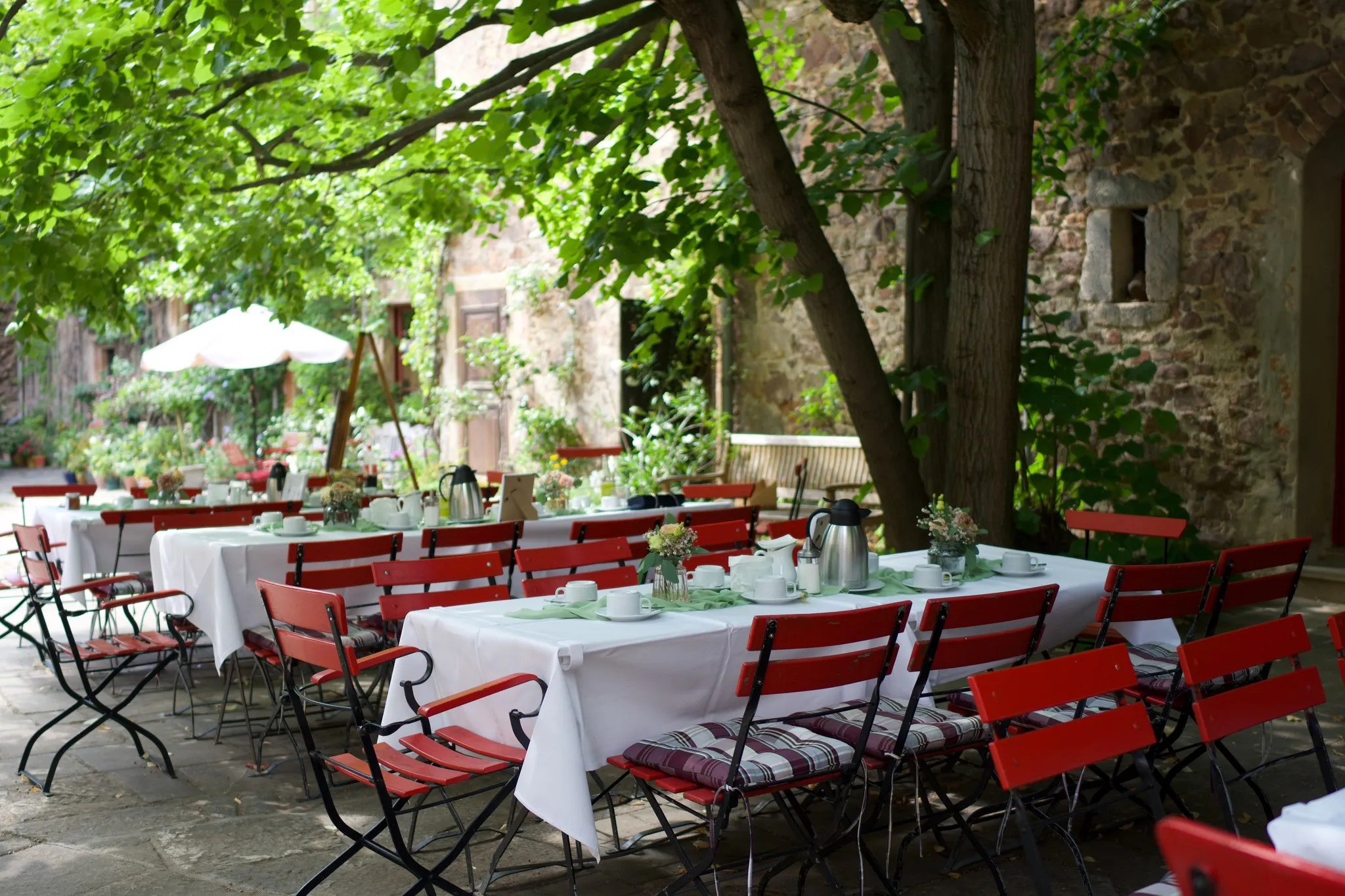 Gedeckte Kaffeetafeln im Schlosshof von Schloss Scharfenberg unter alten Bäumen an der Bruchsteinmauer