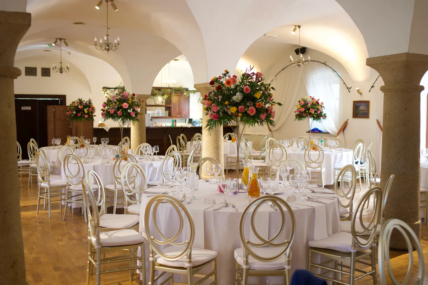 Gewölbesaal mit Säulen und Blumenschmuck, für eine Hochzeit eingedeckt