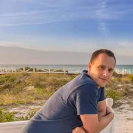 Jan Windisch lehnt an einem weißen Holzgeländer am Strand