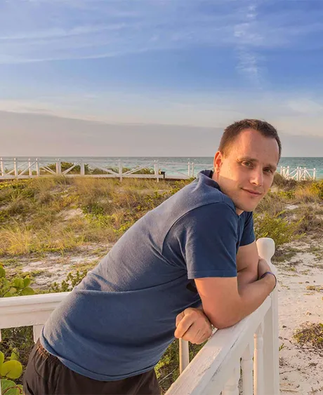 Jan Windisch lehnt an einem weißen Holzgeländer am Strand