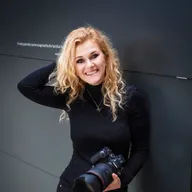 Astrid Flohr lächelt mit Kamera vor dunkler Wand