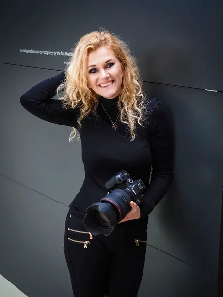 Astrid Flohr lächelt mit Kamera vor dunkler Wand