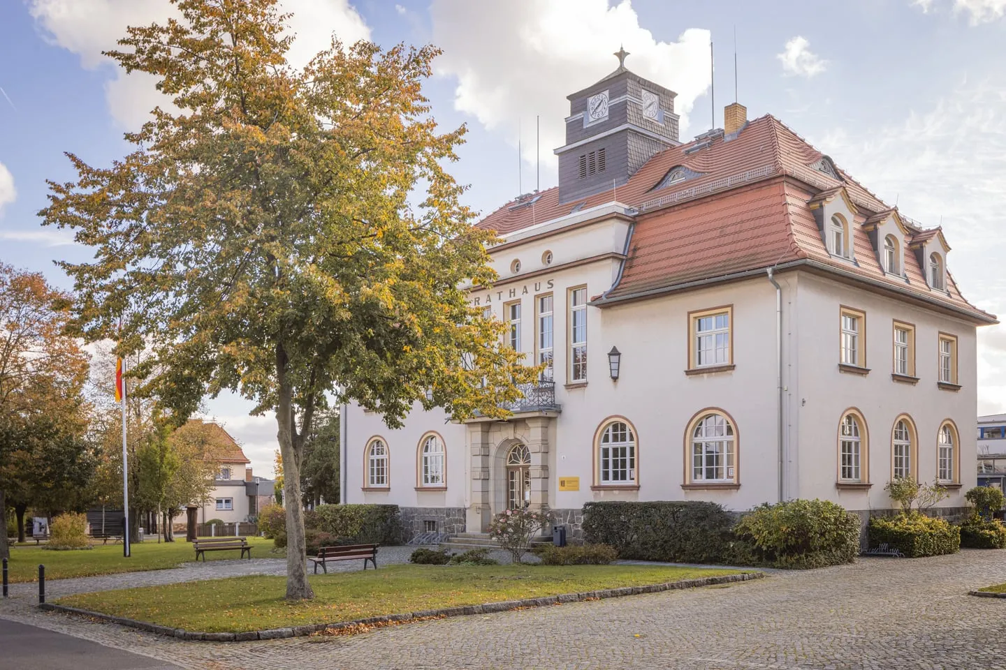 Rathaus Weixdorf mit Uhrturm, rotem Mansarddach und dem Schriftzug „Rathaus“ über dem Eingang, davor herbstliche Bäume und Bänke